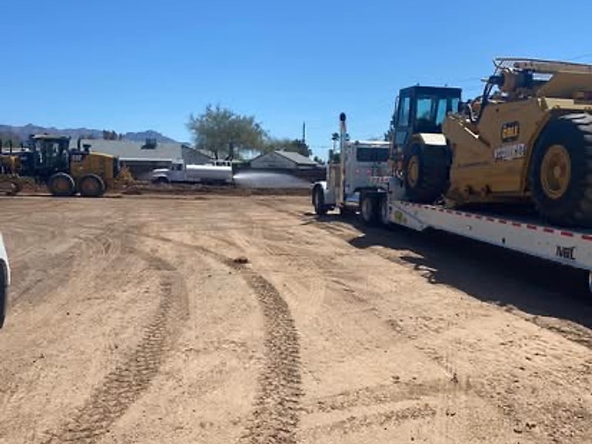 Mighty Earthworks truck hauling a scraper on a flatbed trailer at an Arizona jobsite